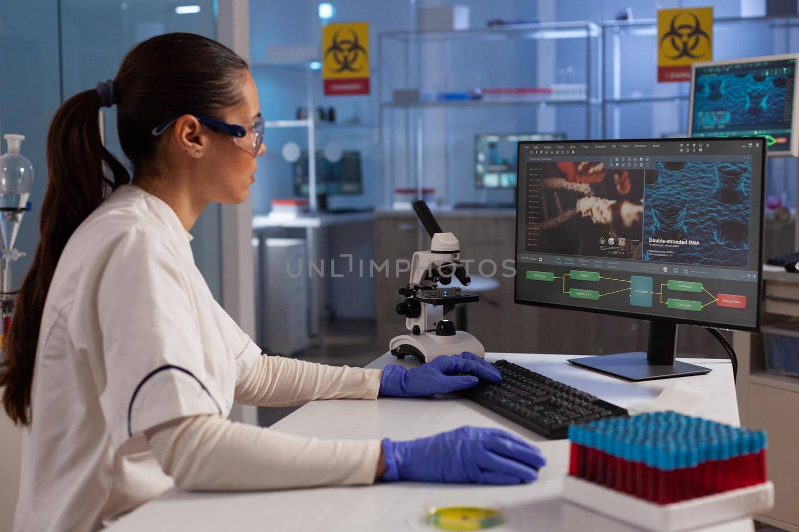 Science specialist using computer for dna research in microbiology laboratory. Professional woman working with illustration of plasma, cell tissue, bacteria invasion, hemoglobin diagram