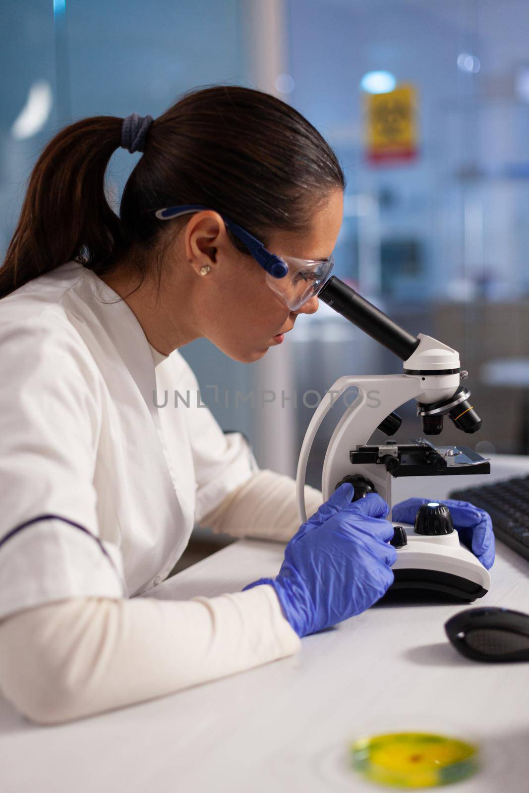 Biochemist working on microscope for cell illustration on computer screen in chemical laboratory. Scientist woman analyzing virus dna, cell tissue, diagram of plasma and hemoglobin nucleus