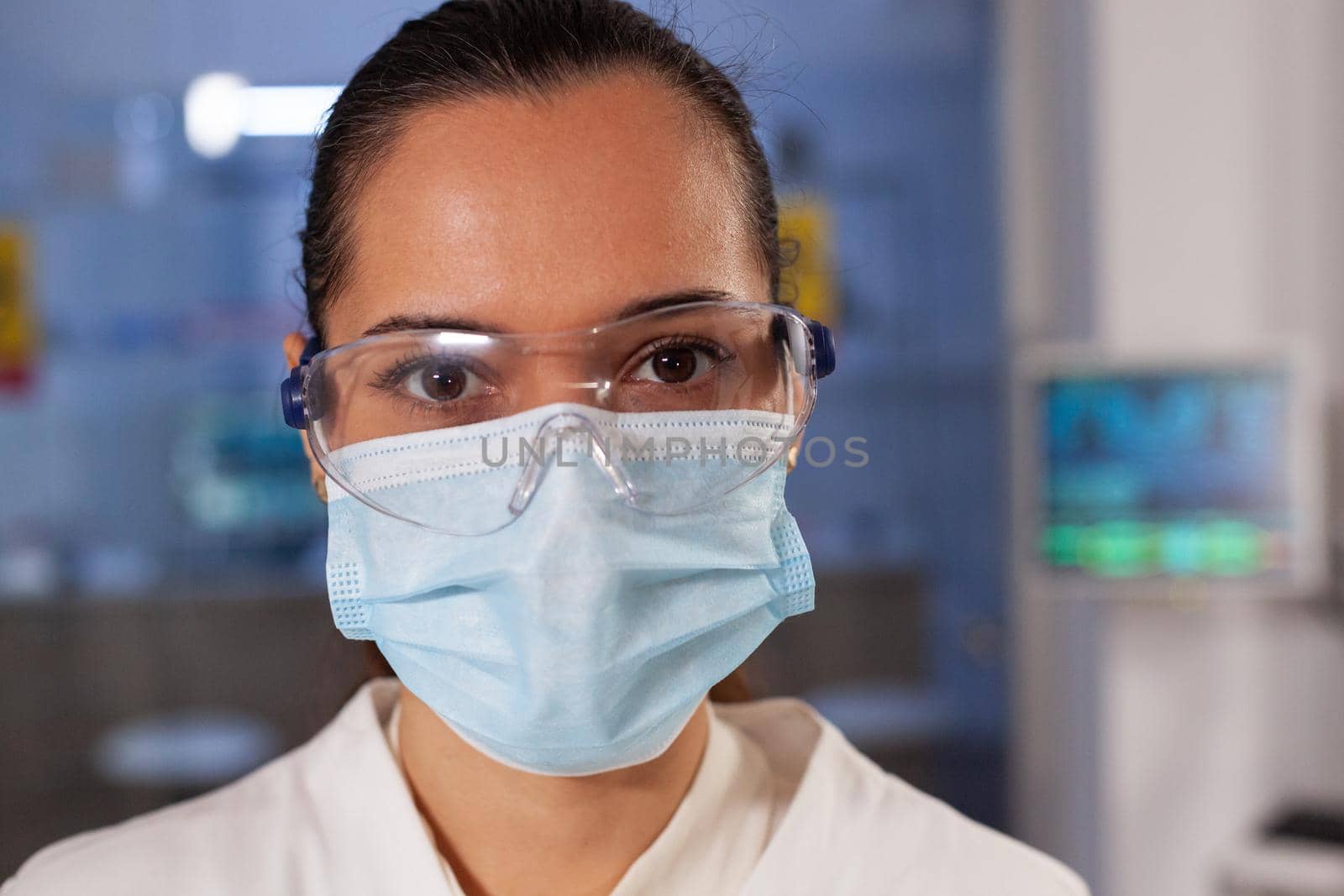 Portrait of biotechnology chemist working in laboratory at medical hospital. Woman with scientist occupation wearing protection glasses, face mask and lab coat industry equipment