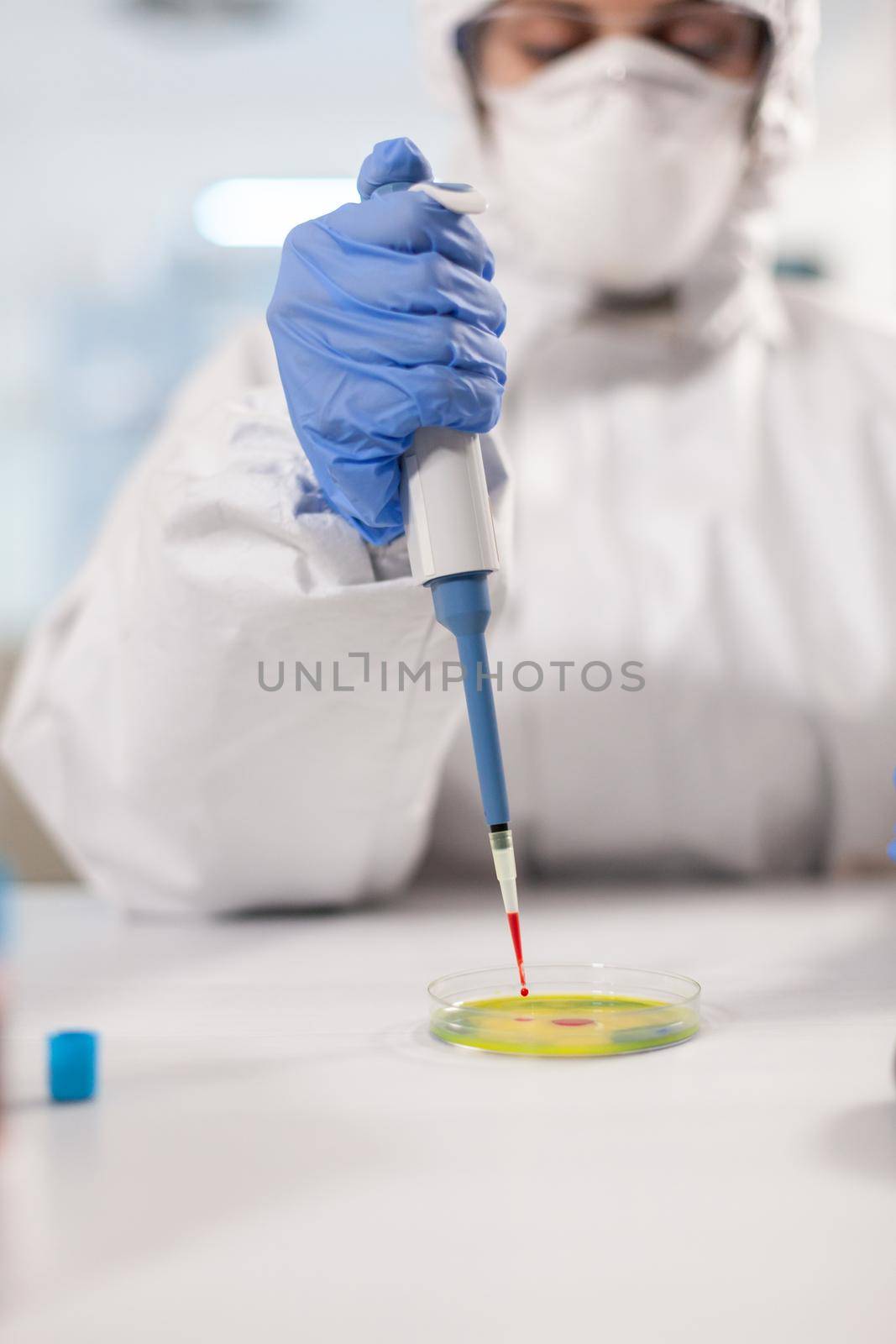 Scientist working to develop virus treatment dressed in ppe suit using micropipette. Chemist in coverall working with various bacteria, tissue blood samples for antibiotics research.