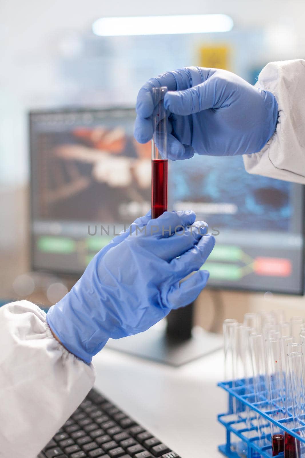 Close up of scientist hands dressed in ppe suit holding blood test tube. Team doctors working with various bacteria, tissue and blood samples, pharmaceutical research for antibiotics.