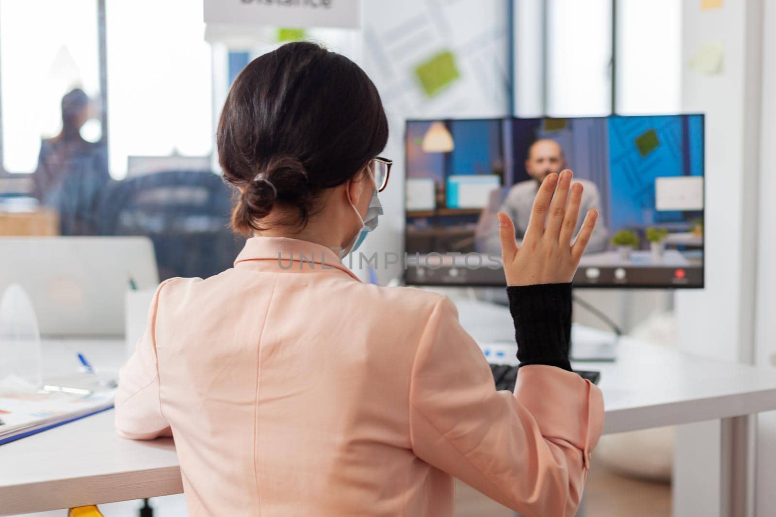 Woman discussing job project with business man during remote video call in new normal office in time of global pandemic with covid19, wearing face mask safety prevention against infection.