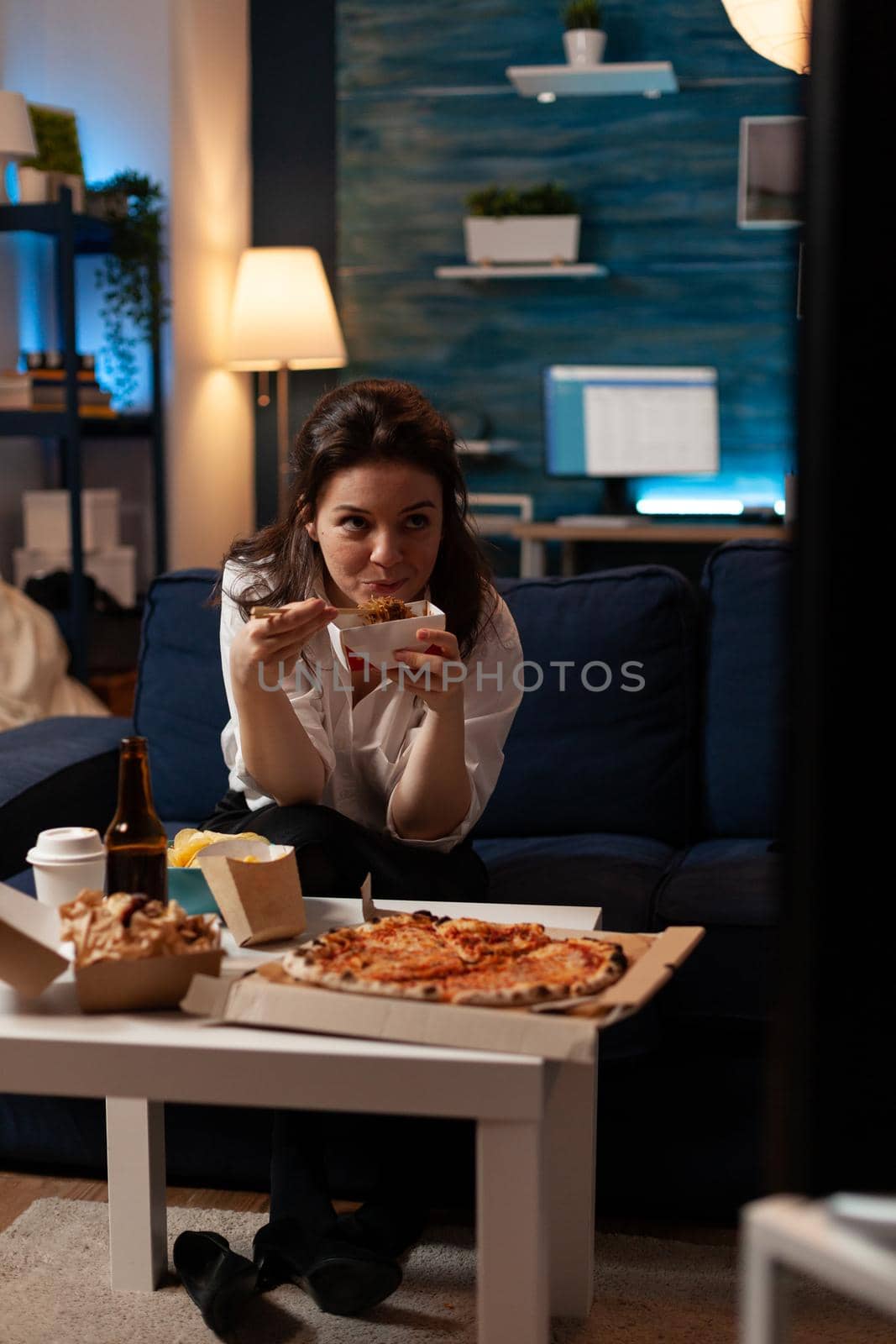 Caucasian female watching entertainment movie on television during takeaway food delivery in evening. Woman eating tasty delicious chinese-food relaxing on sofa enjoying unhealthy night