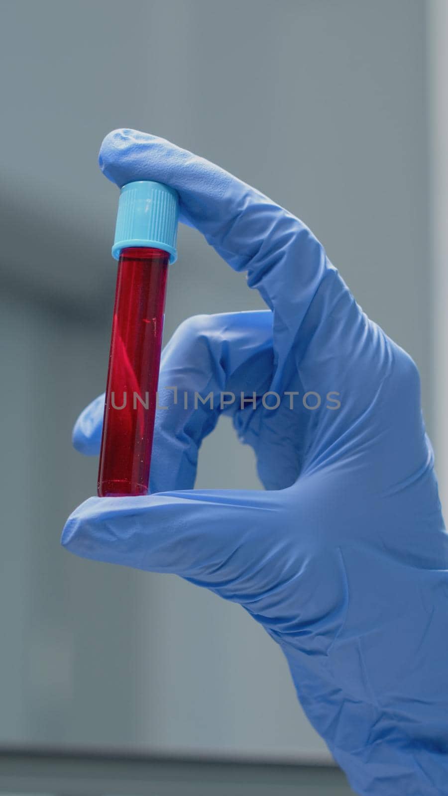 Close up of specialist hand with gloves holding vacutainer with red solution or blood in research laboratory. Glass science instrument with liquid in transparent beaker used for innovation