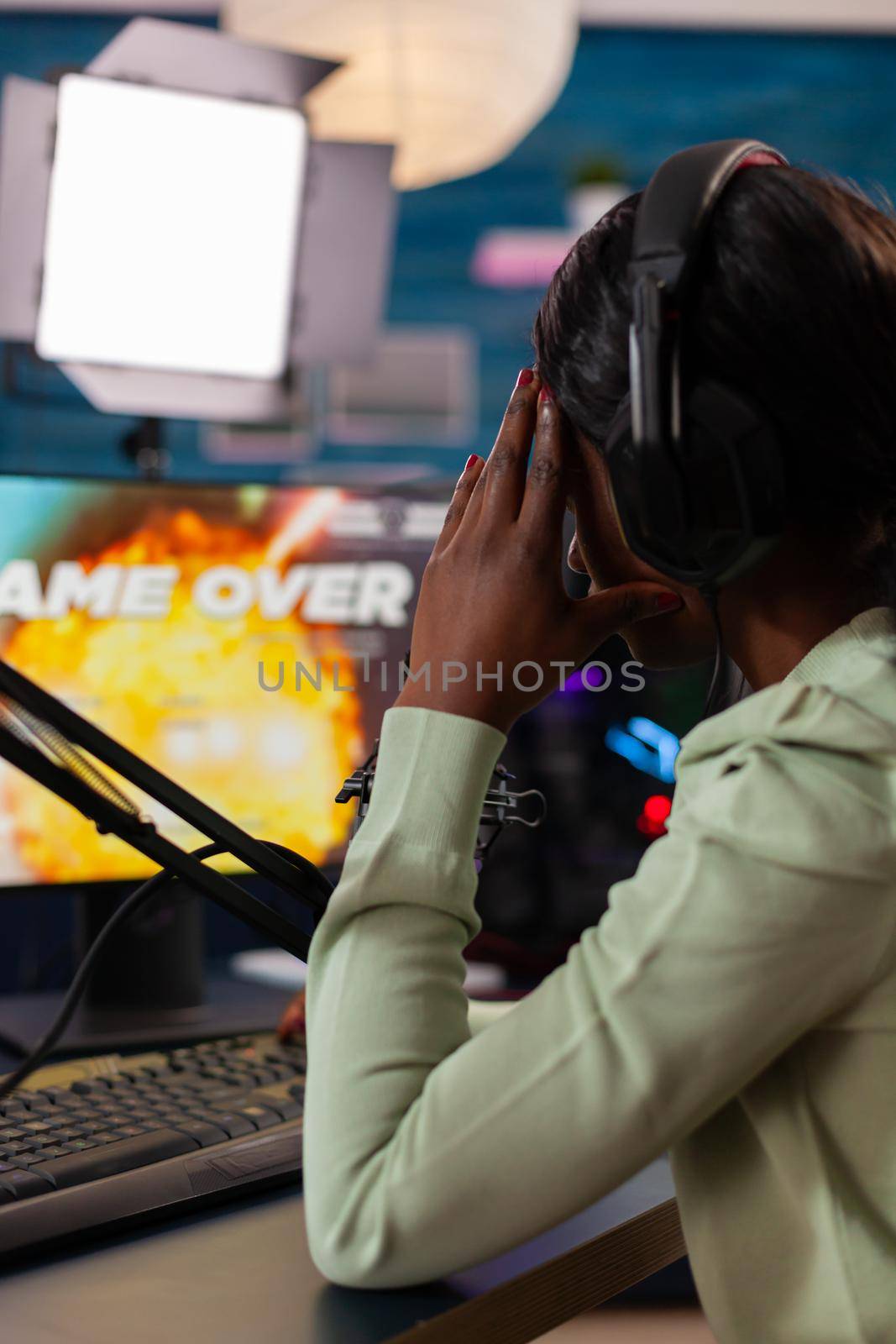 Back shot of afro american esport streaming losing virtual competition wearing headphones.Professional gamer streaming online video games with new graphics on powerful computer.