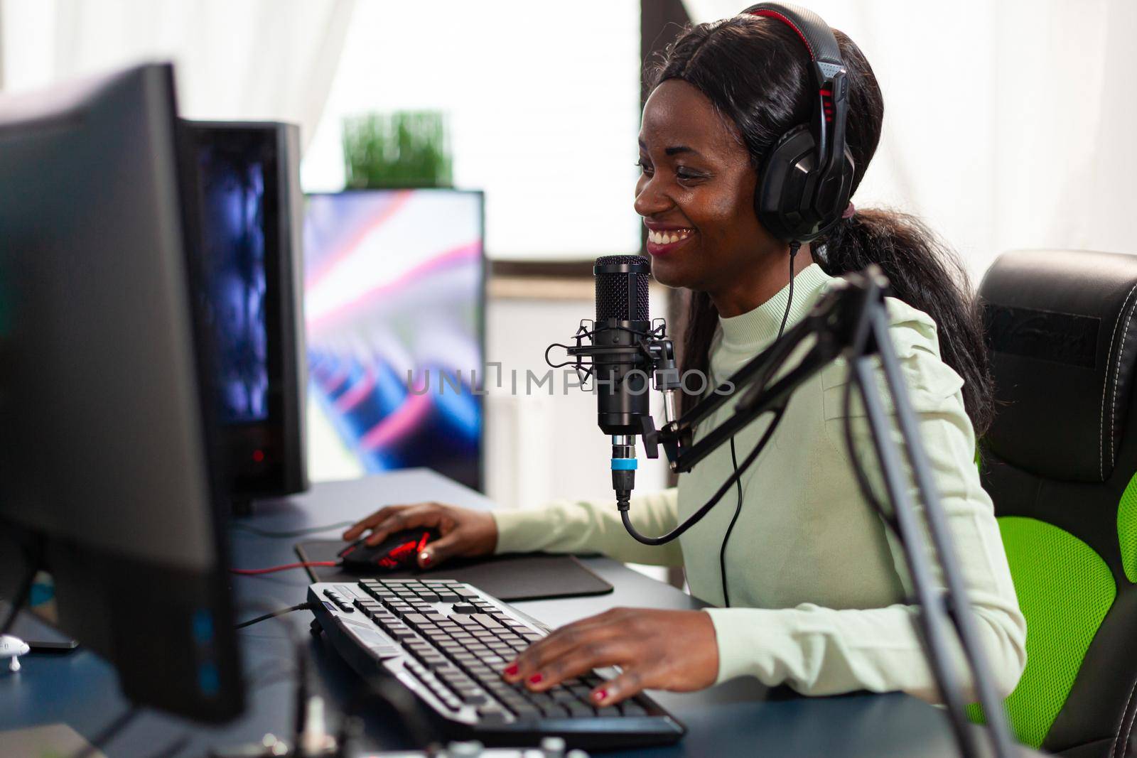 Smiling esports streamer wearing headphones ejoying live competiton sitting on chair. Streaming viral video games for fun using headset and keyboard for online championship.