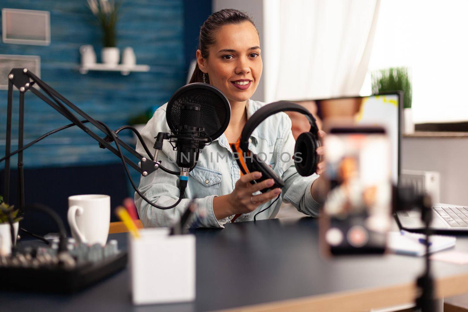 Influencer presenting headphones for giveaway to camera while making video blog in home studio by DCStudio