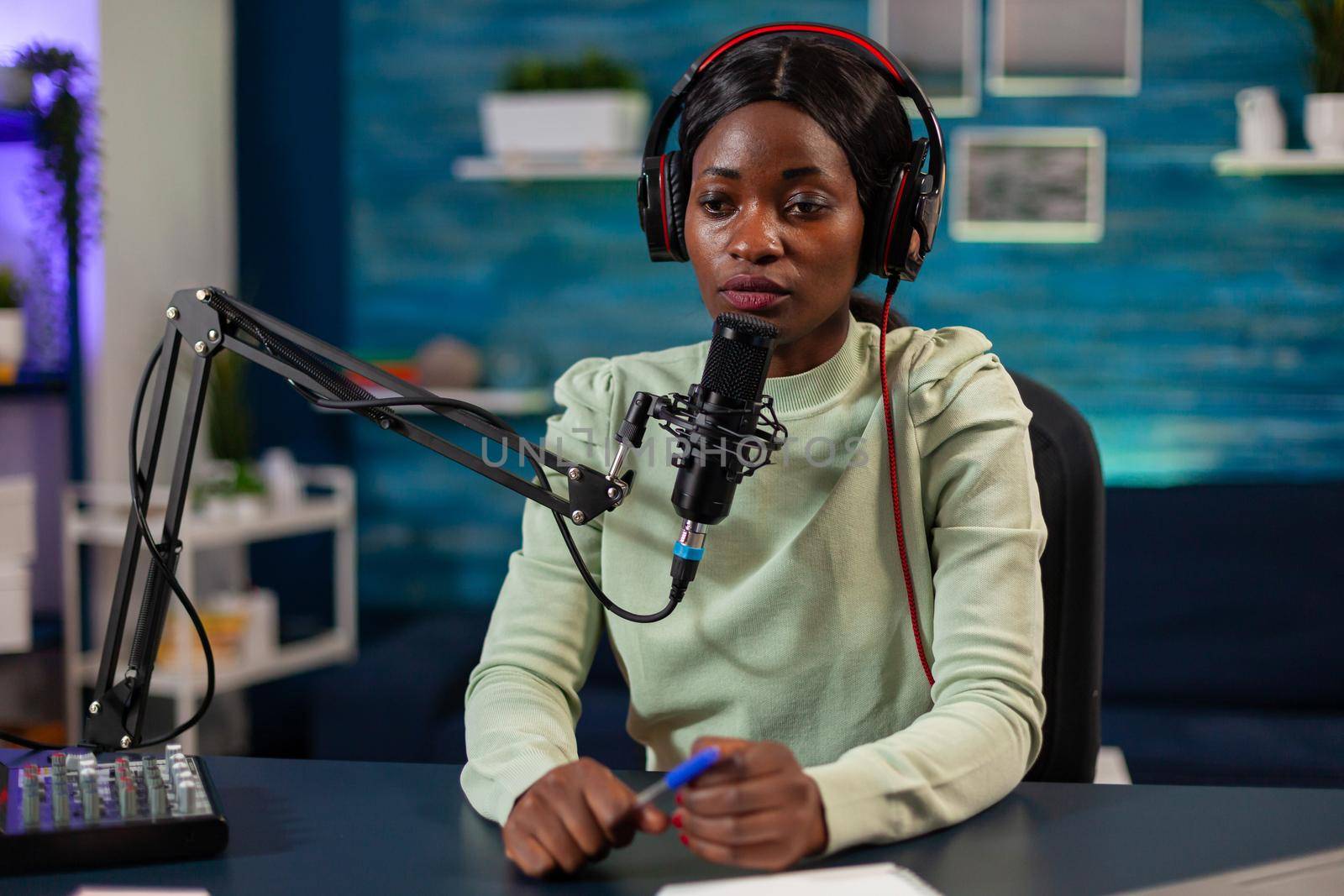 African woman host of online show talking into microphone wearing headphones. Speaking during livestreaming, blogger discussing in podcast wearing headphones.