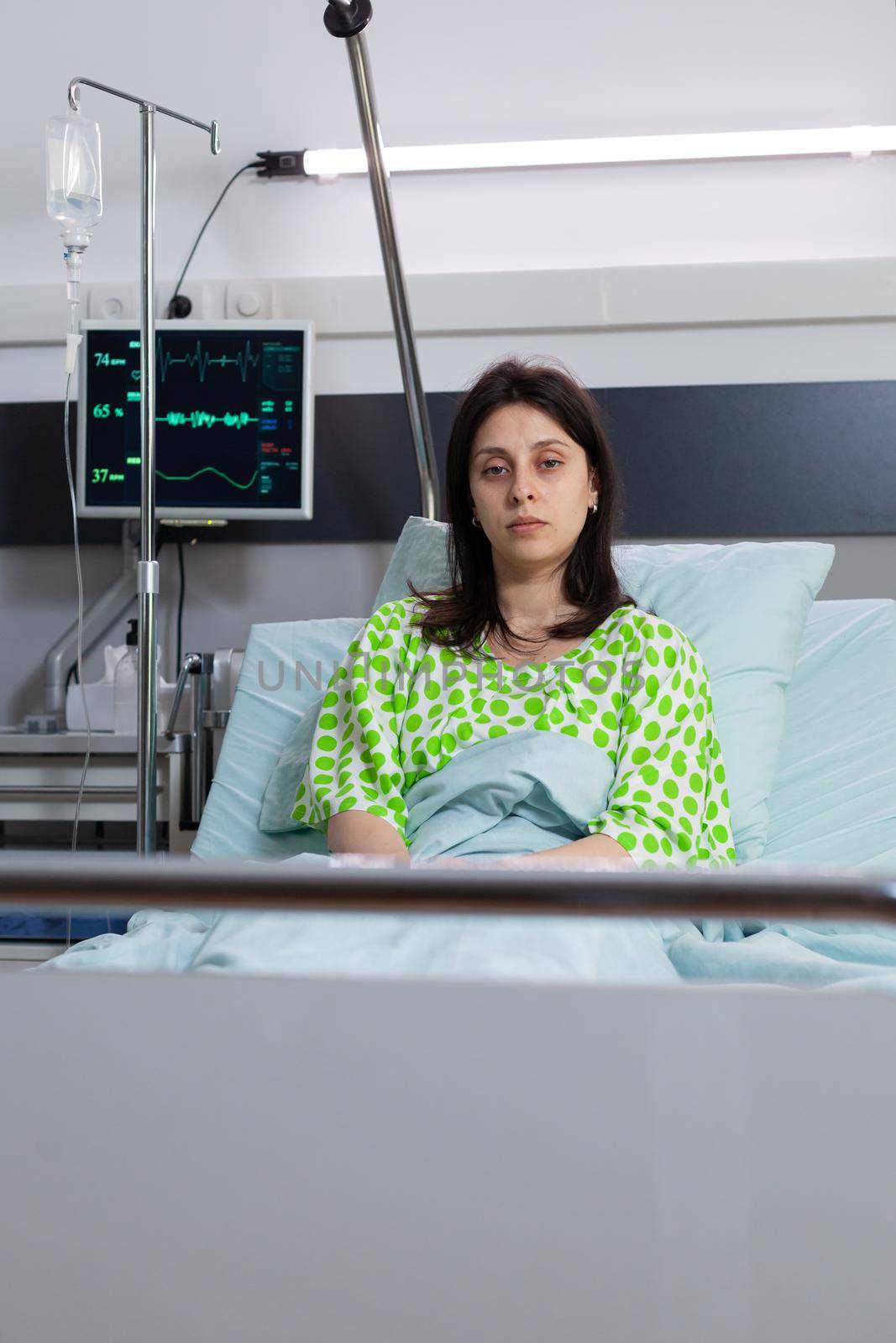 Hospitalized sick woman with nasal oxygen tube looking into camera resting in bed recovering after respiratory surgery. Patient with breathing disorder waiting for sickness treatment in hospital ward