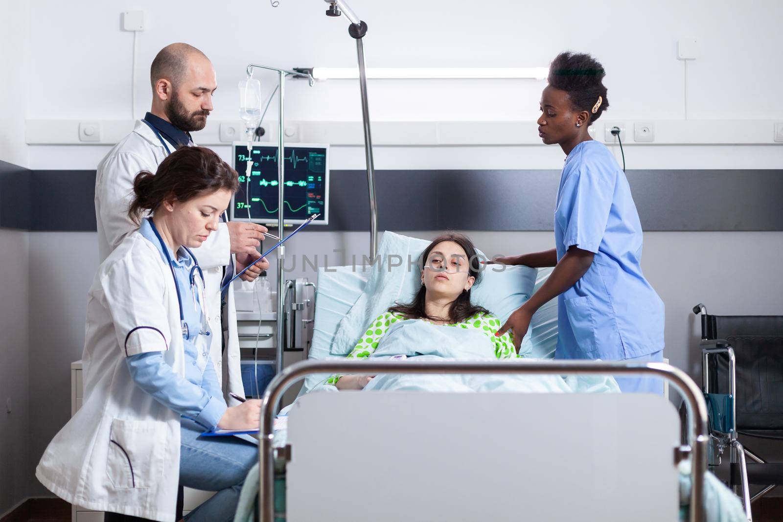 Practitioner doctors monitoring disease symptom writing recovery treatment on clipboard during medical appointment in hospital ward. Sick patient resting in bed recovering after surgery