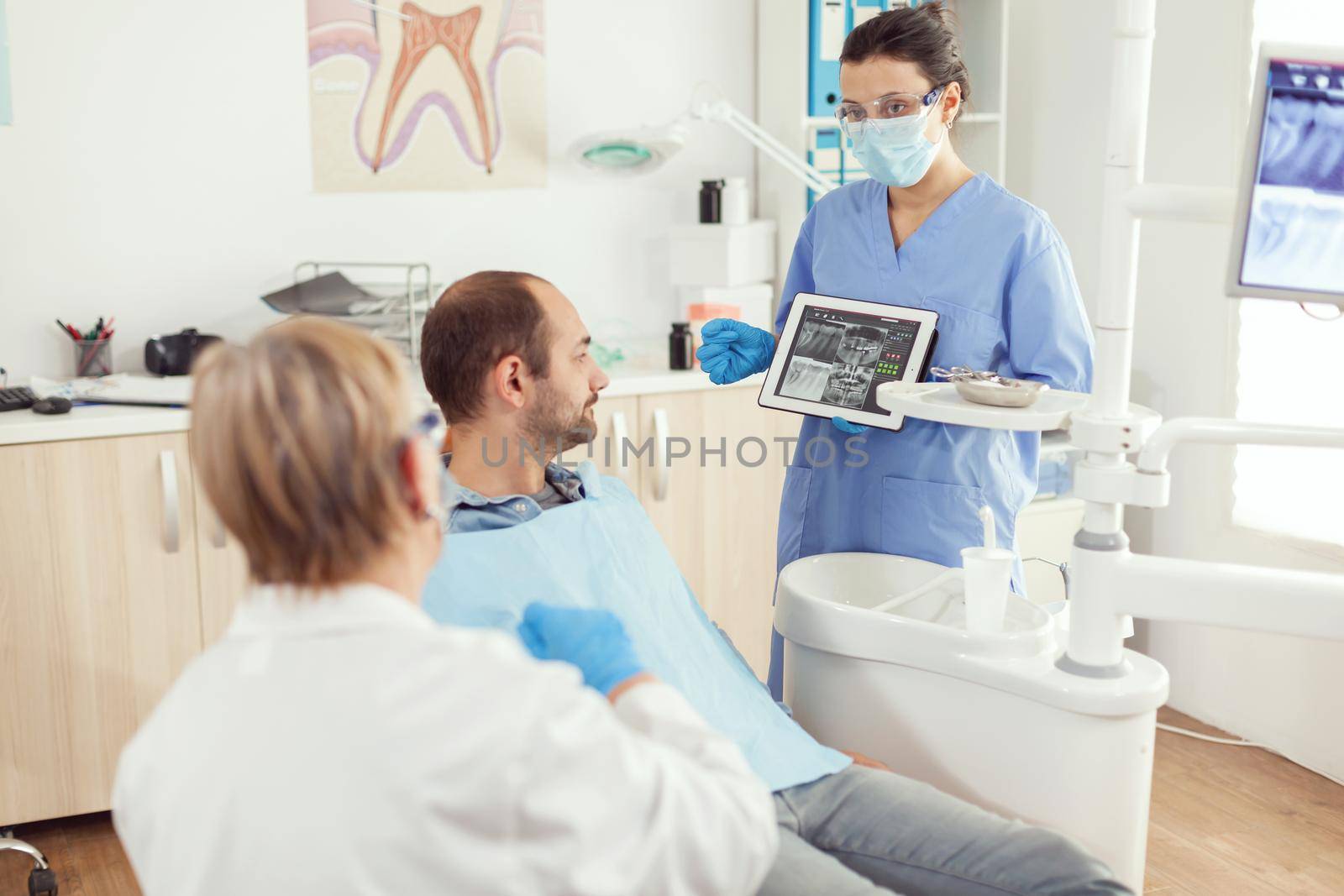 Stomatology nurse in dentistiry office showing tablet pc with tooth radiography by DCStudio