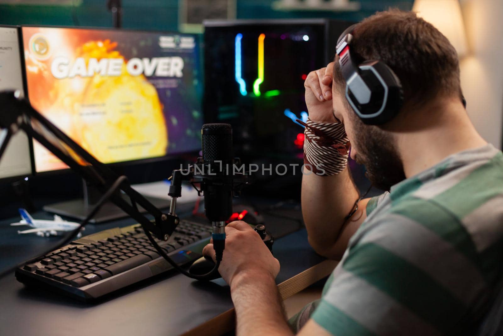 Videogame streamer losing videogame competition while wearing professional headset. Defeated gamer using modern controller for online tournament late at night in gaming room