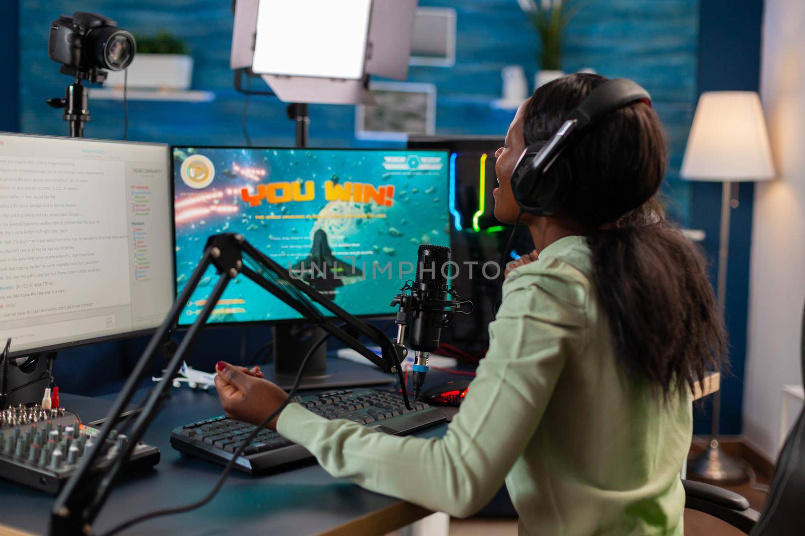 African video games e sports player screaming after wining championship while streams the play talking on microphone. Online streaming cyber performing during video games tournament in home with neon lights.