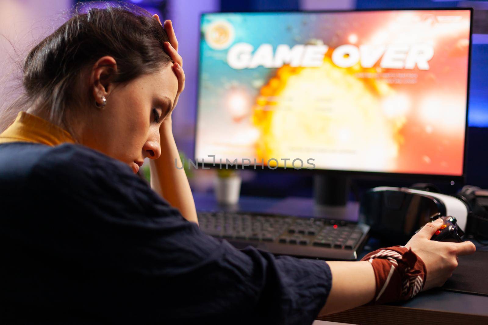 Pro videogames keeping his head on hand after losing space shooter game using wireless joystick . Defeated gamer wearing vr headphone for online championship sitting on gaming chair late at night