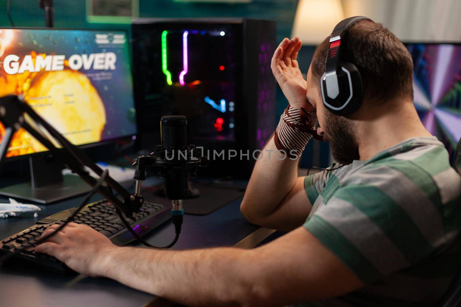 Back shot of disappointed esport streamer losing virtual competition videogame using modern headphone. Professional gamer streaming online video games with new graphics on powerful computer