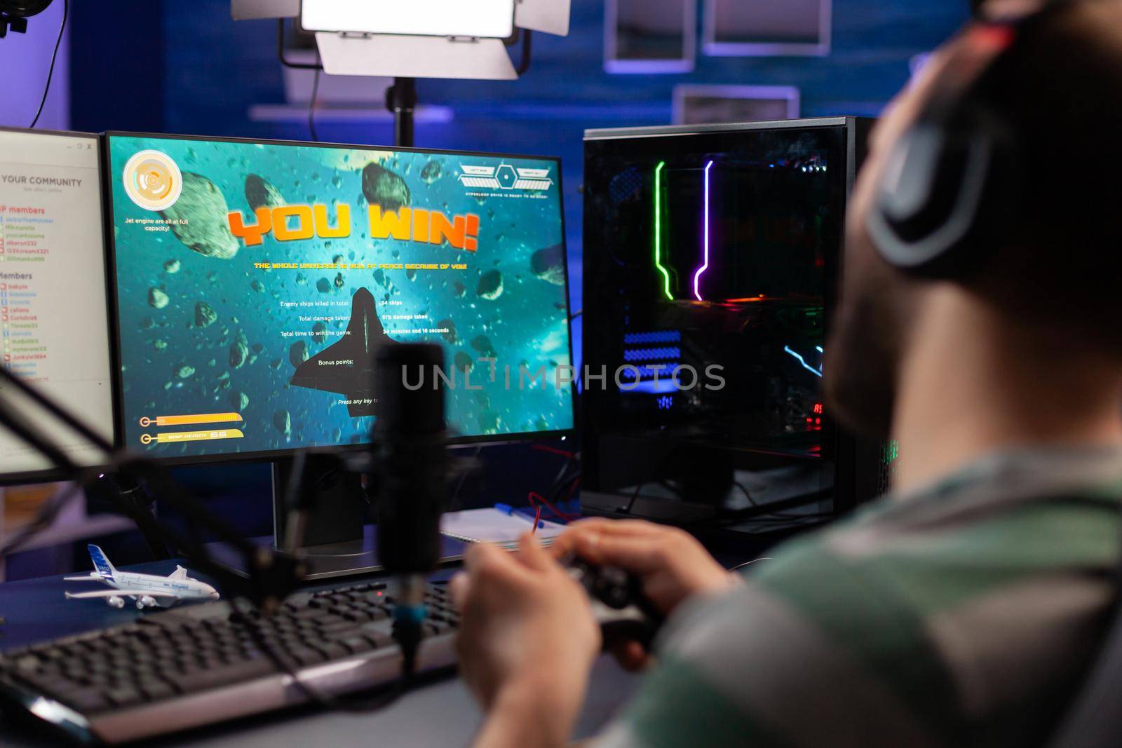Excited streamer winning online virtual game competition of space shooter playing on powerful computer. Professional gamer using joystick for space shooter championship sitting on gamining desk