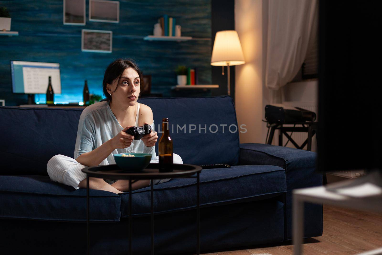 Focused defeat gamer playing video games on tv late night trying to win online soccer competition using gaming joystick. Involved serious woman sitting on couch relaxing in living room