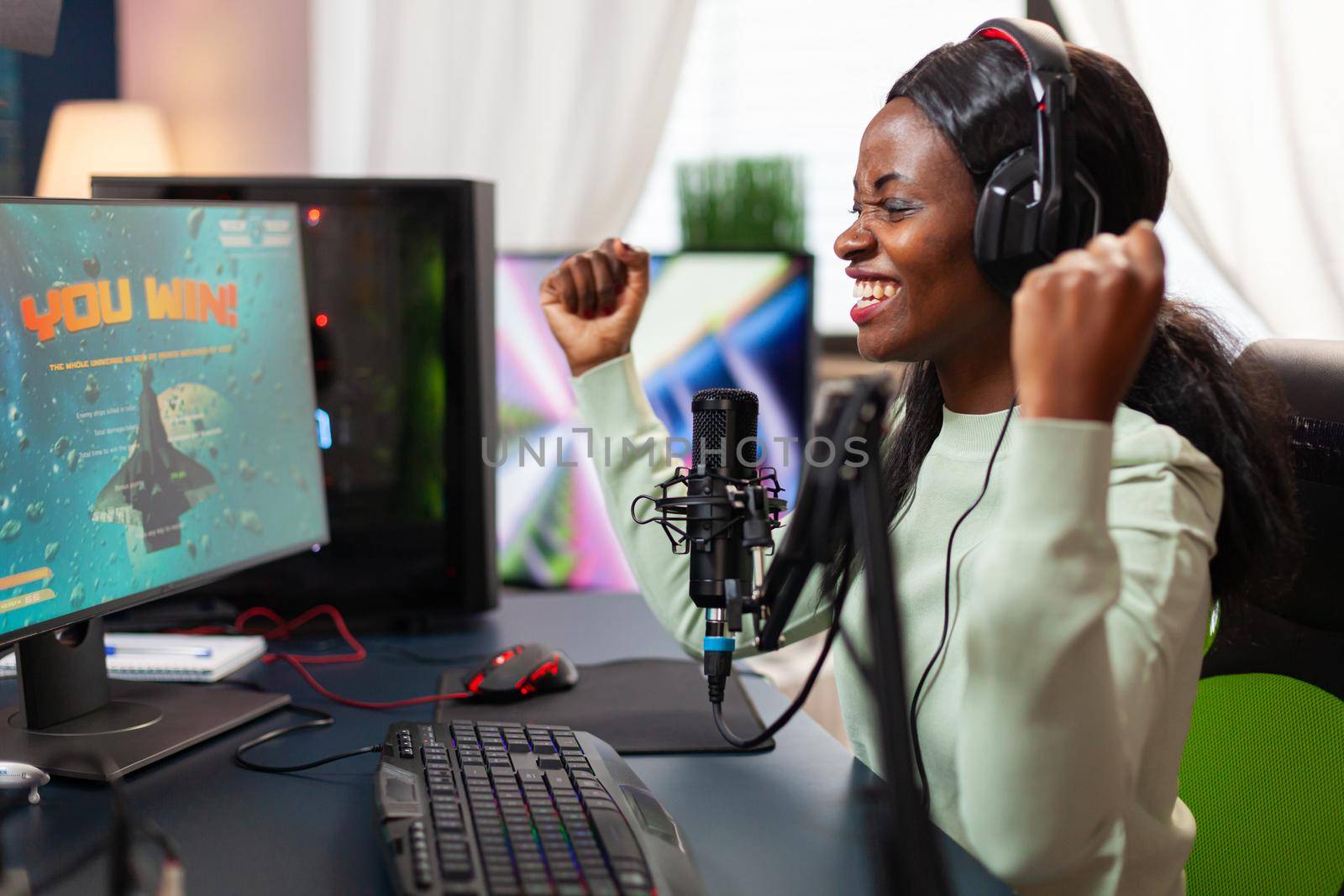 Pro african esport streamer excited after wining video games championship screaming into microphone. Online streaming cyber performing during video games tournament in home with neon lights.