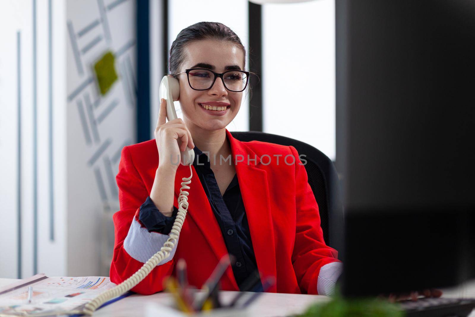 Businesswoman having a phone coversation with financial adviser sitting at desk looking at charts on computer screen. Company executive answering taking a cellphone call.