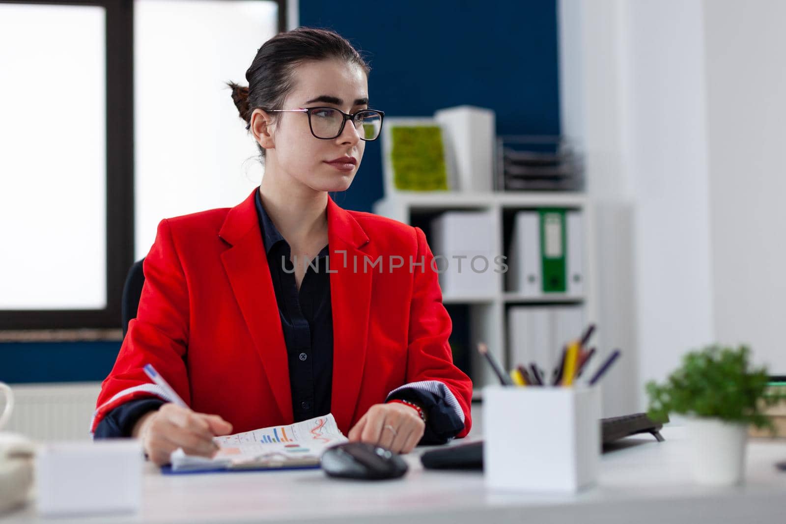 Employee in business corporate office workplace looking at computer screen and taking notes on clipboard, about financial money analysis. Entrepreneur broker checking company revenue.