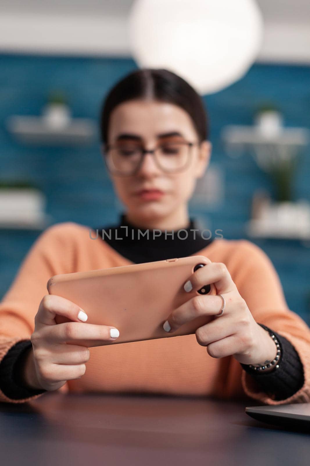 Close up of player hands holding smartphone in horizontal mode during online shooter competition. Competitive gamer sitting at desk table in living room, mobile video games tournament