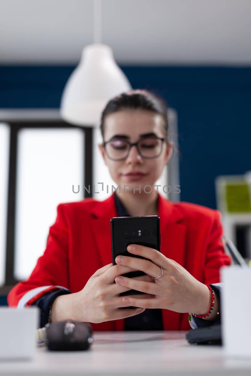 Selective focus on smartphone while businesswoman is texting, to her assistant. Wwworking in corporate office reading text on cellphone and messeging answer. Business executive using mobile.