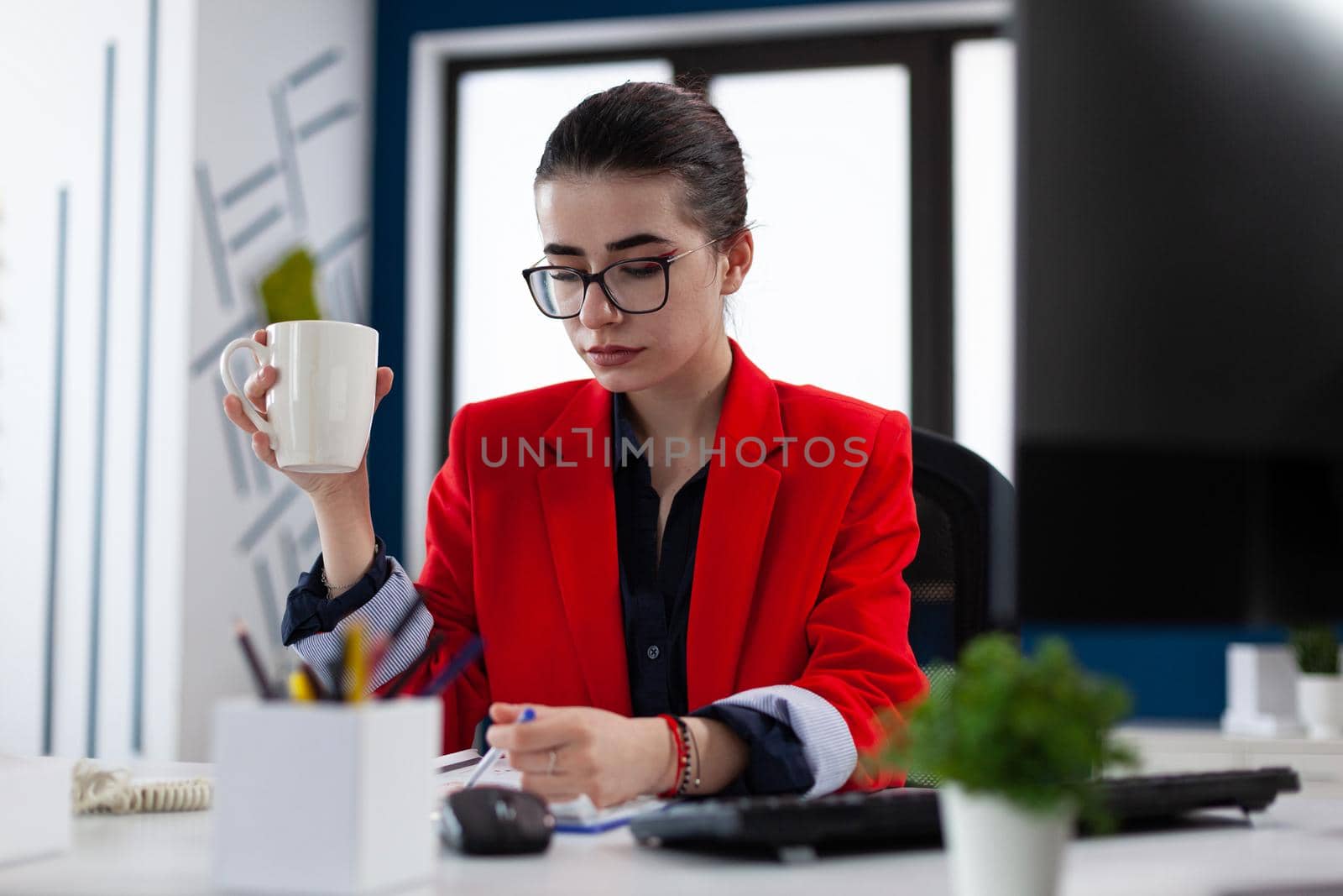 Entrepreneur holding cup of coffee in business workplace office, cheking notes about financial expertise on clipboard. Manager sitting at desk table reviewing strategy. Caffeine addicted.