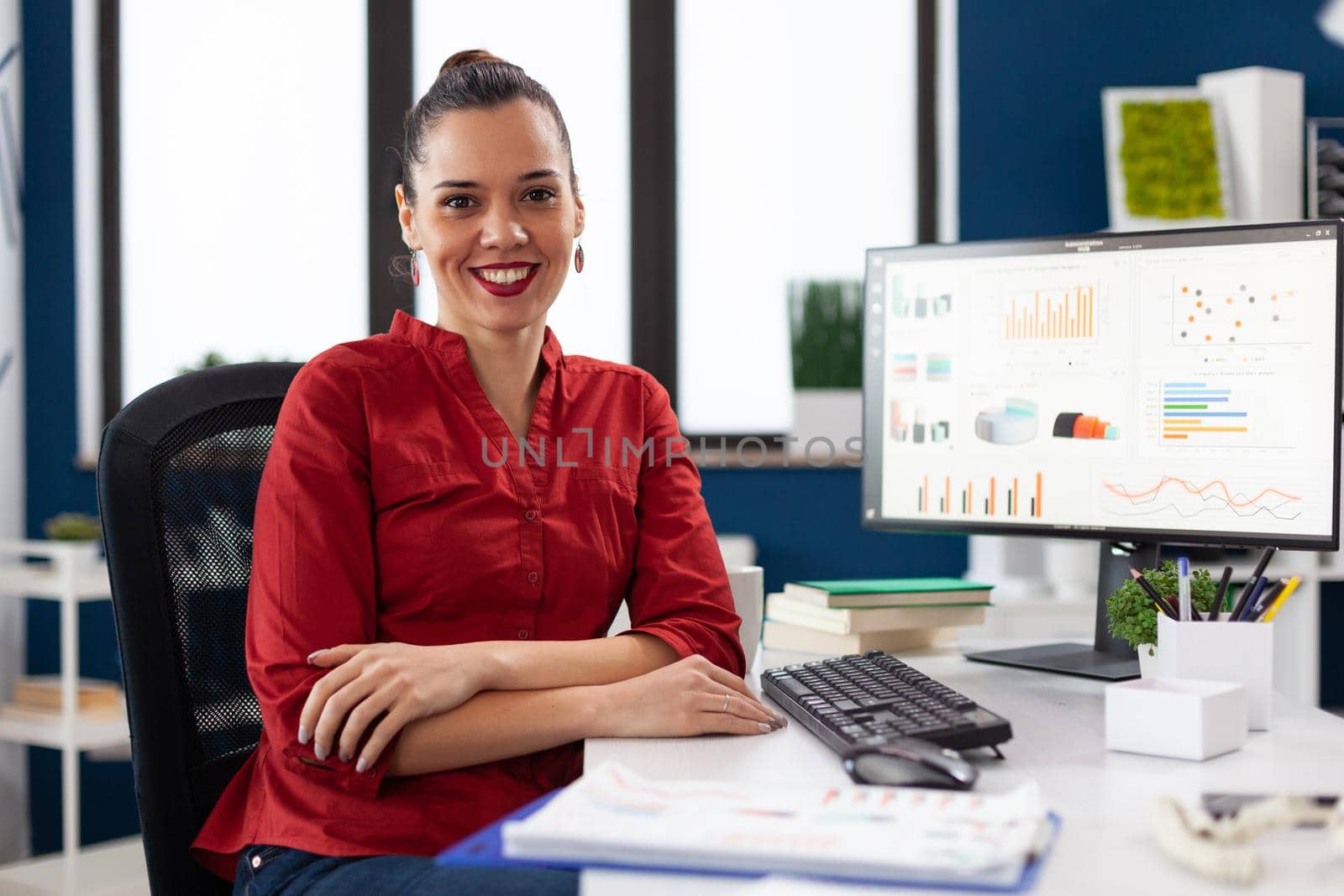 Portrait of business woman in corporate office sitting at desk by DCStudio