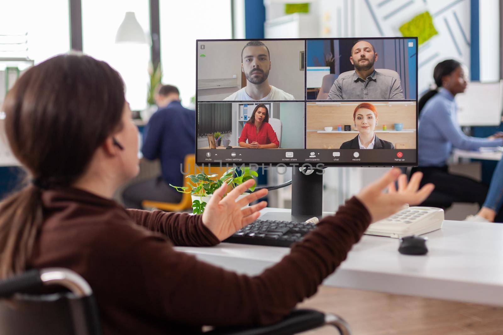 Handicapped amputee paralysed project manager talking with team during video conference using videocall sitting in wheelchair in startup business office. Corporate partner discussing in online meeting.