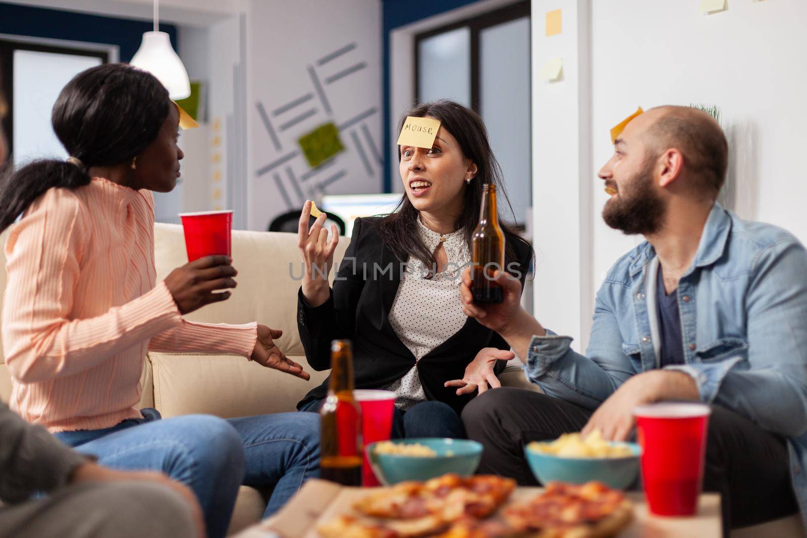 Cheerful group of colleagues enjoying a game of charades after work at office. Multi ethnic people play imitation concept for fun activity entertainment while eating pizza and drinking beer