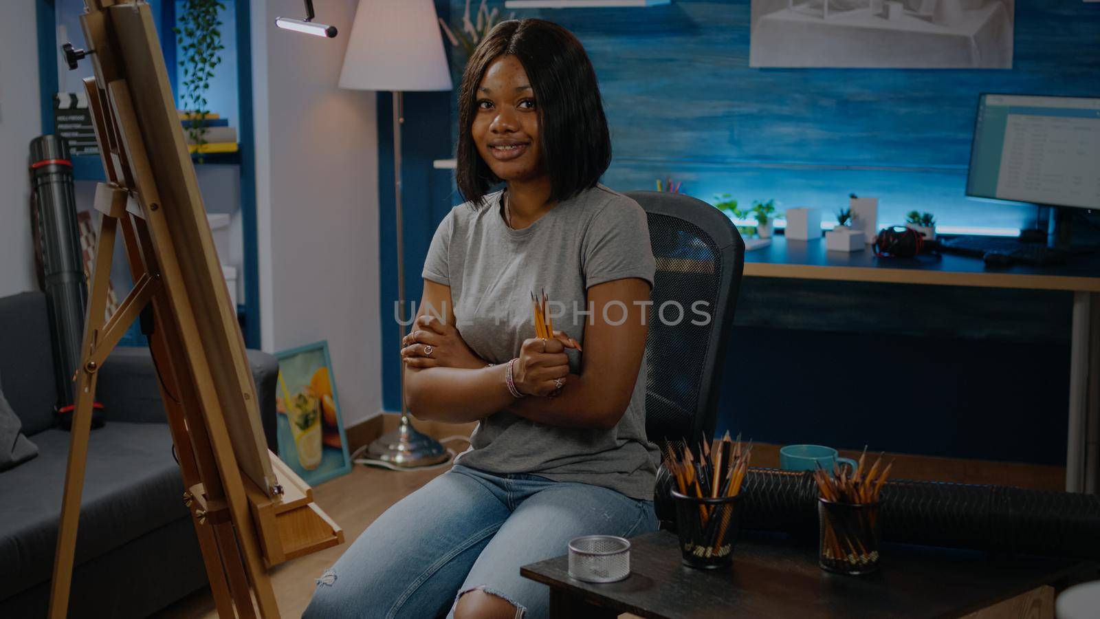 African american young woman holding colorful pencils prepared to draw on white canvas sitting in artwork studio. Black artist with creative inspiration ready for masterpiece design
