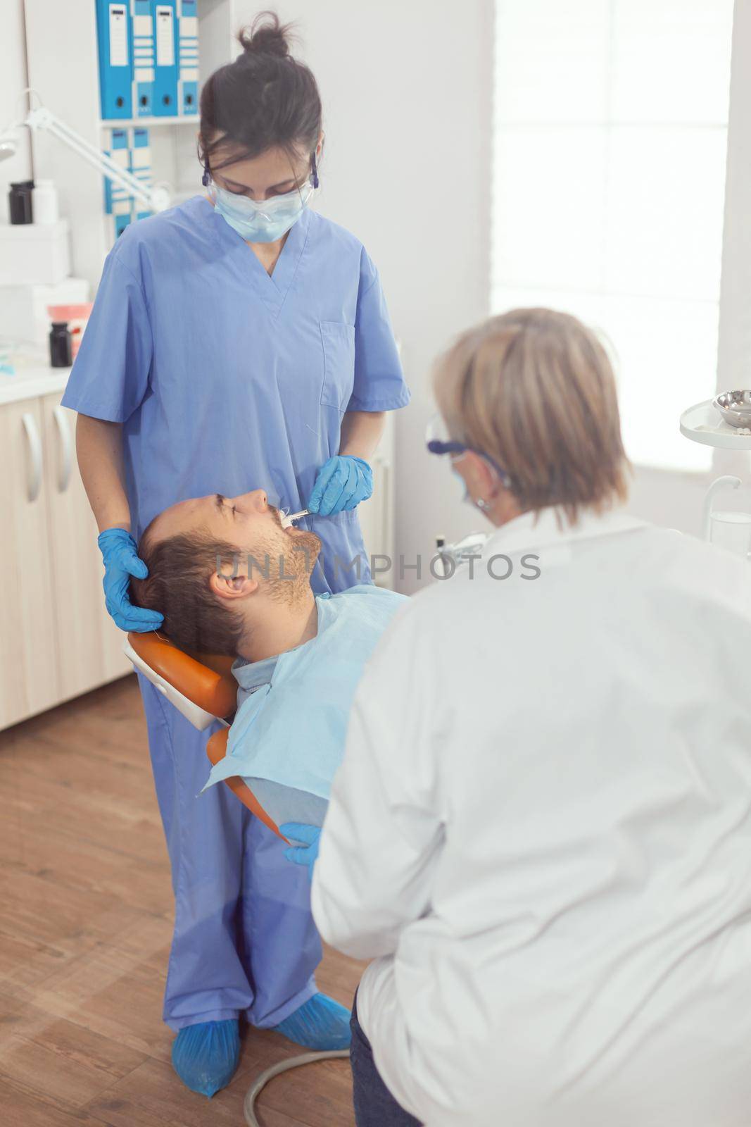 Sick patient lying on dental chair with open mouth for medical procedure by DCStudio