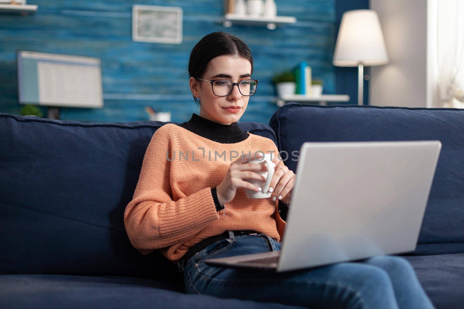 Student looking at laptop computer during online management courses sitting comfortable on sofa in living room. Woman reading marketing lesson on university platform, teenager studying at distance