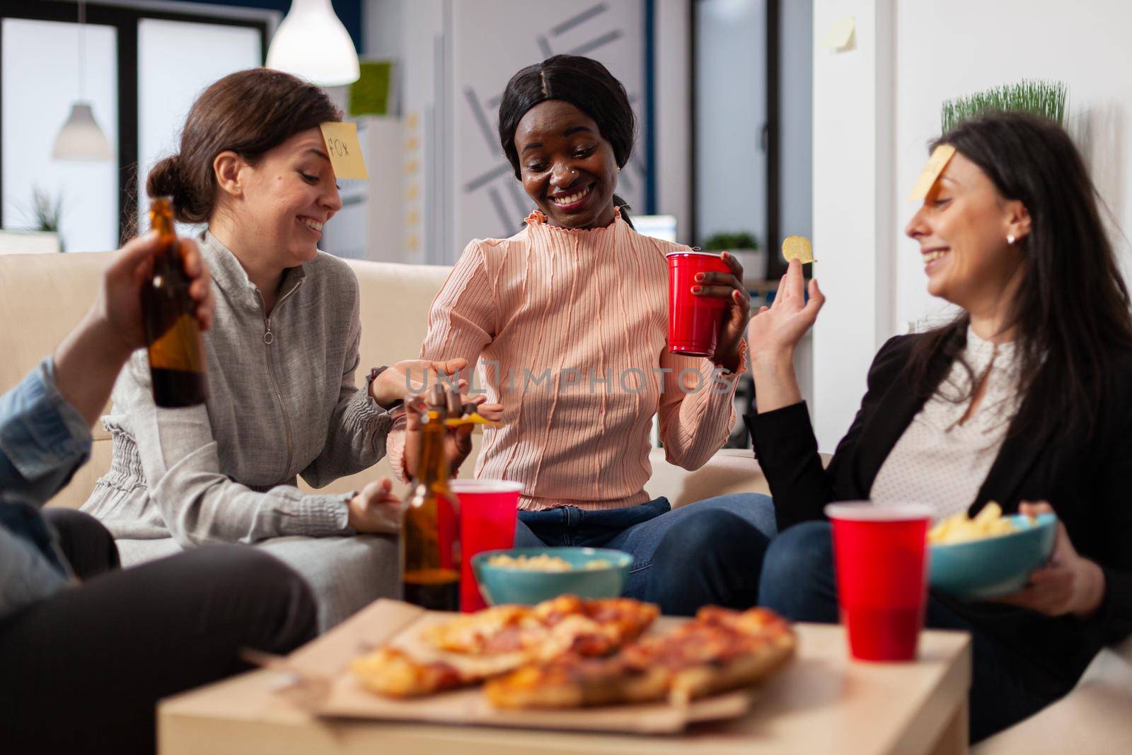 Diverse team of colleagues play game of guessing after work at office while sitting on couch. African american woman doing impersonation for fun cheerful activity entertainment enjoyment