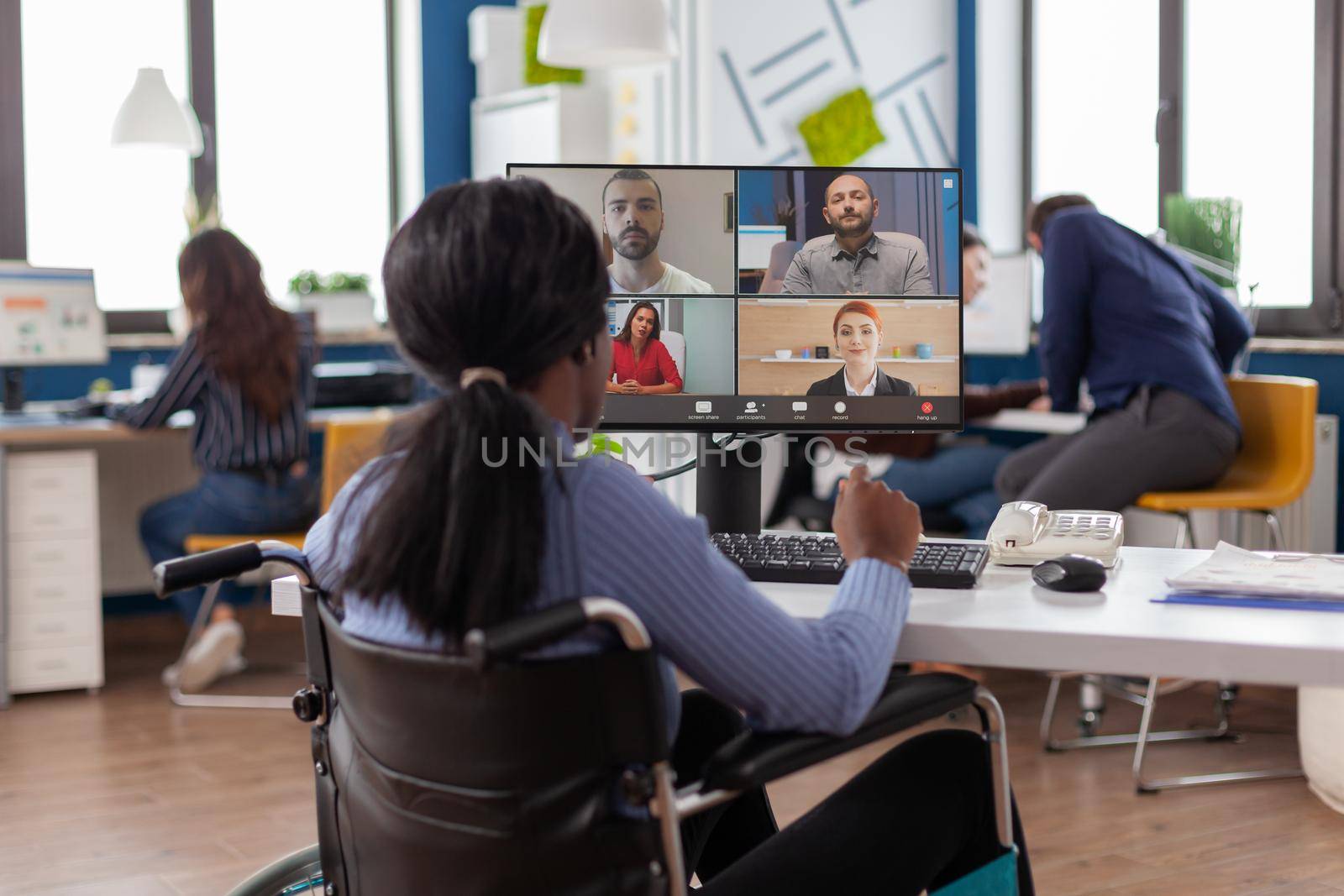 Immobilized black project manager in wheelchair talking on videocall during online meeting discussing with business partners working in financial company, start up office with modern technology.
