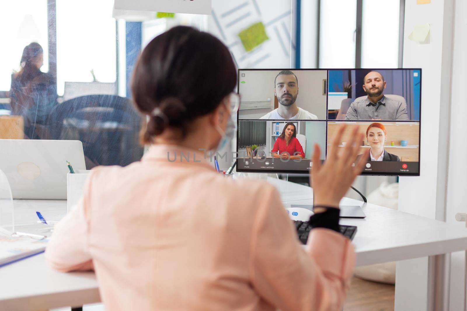 Businesswoman talking remotely with freelancers in corporate office workplace wearing face mask as safety prevention, keeping social distancing wearing face mask.