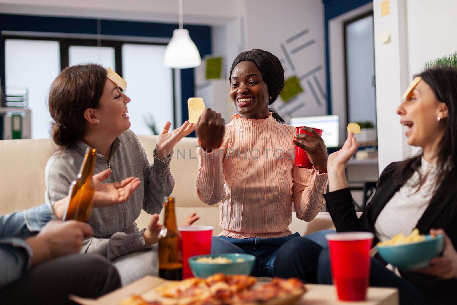 Diverse team of colleagues play game of guessing after work at office while sitting on couch. African american woman doing impersonation for fun cheerful activity entertainment enjoyment