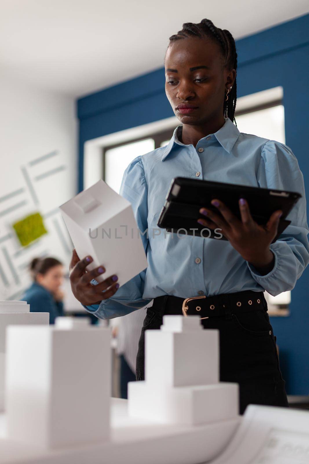 Person of african american ethnicity working as architect in professional environment. Woman at office looking at tablet for building model design plan maquette. Engineer work environment