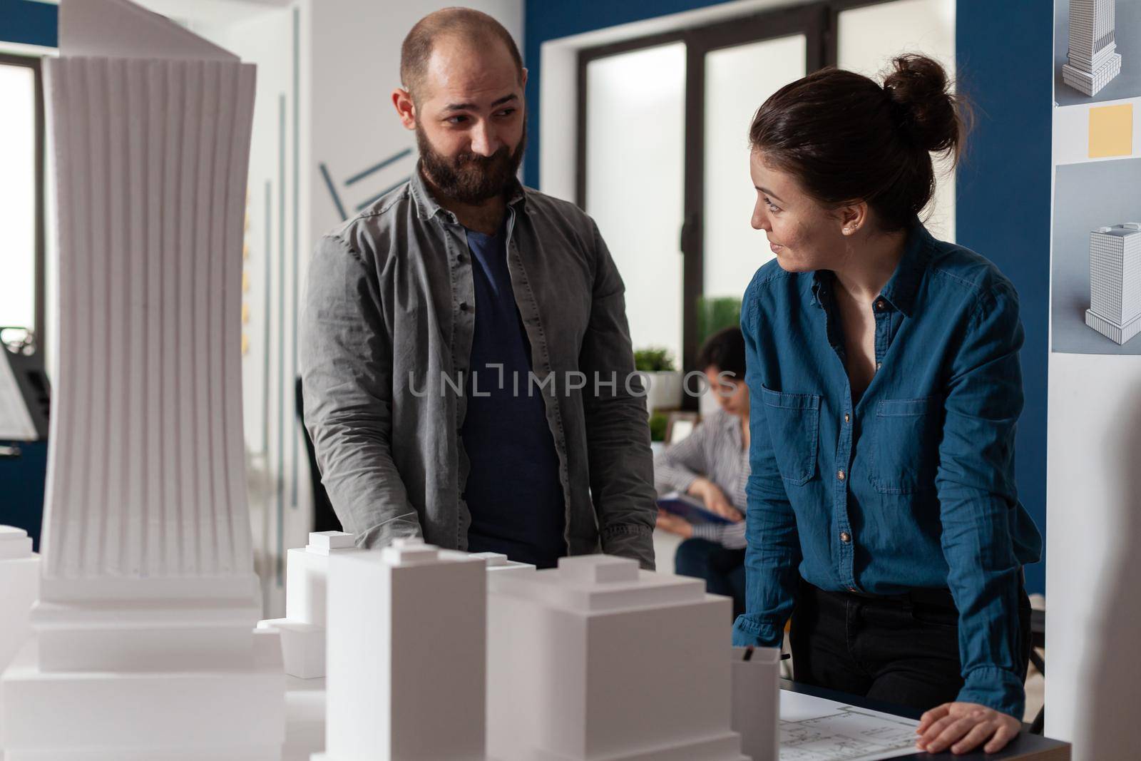 Architect work team talking at professional office standing at desk with maquette building model. Caucasian project partners looking to design blueprint for construction layout