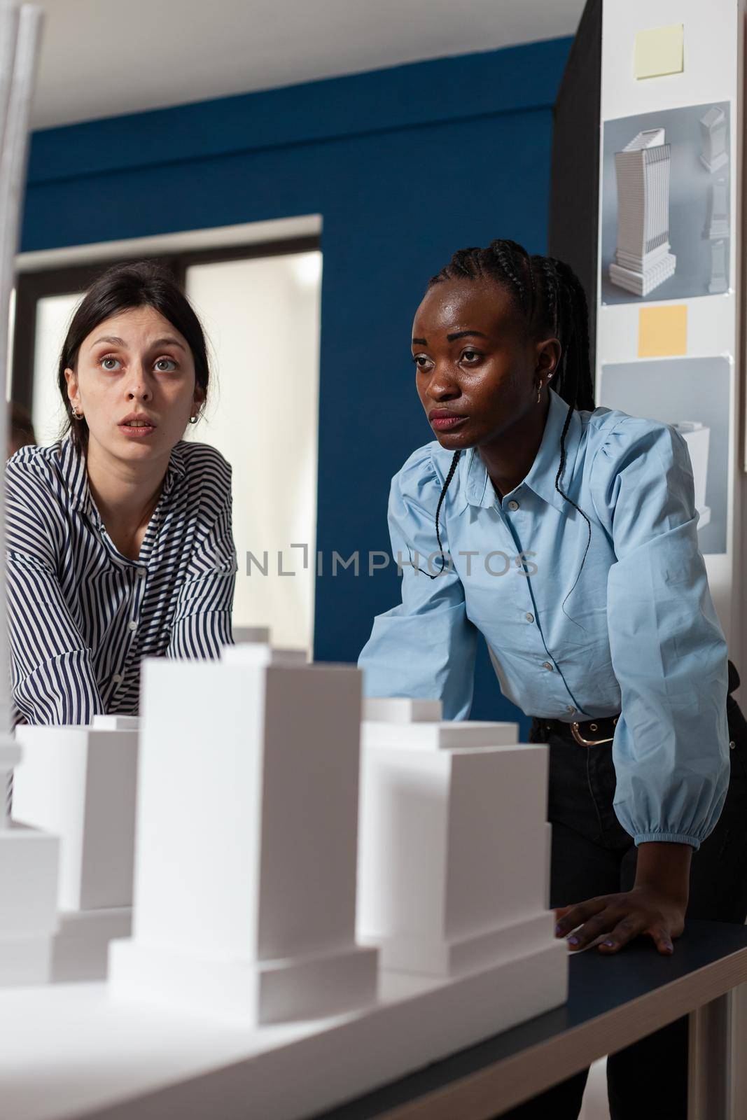 Professional architecture multi ethnic women working on blueprints and building model maquette construction design. Team of workers pointing at architectural paper plan as occupation