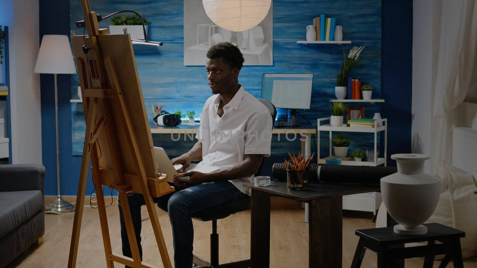 Artist of african american ethnicity using laptop computer in creative studio for inspiration and drawing design. Black person creating fine art masterpiece for innovative imagination concept