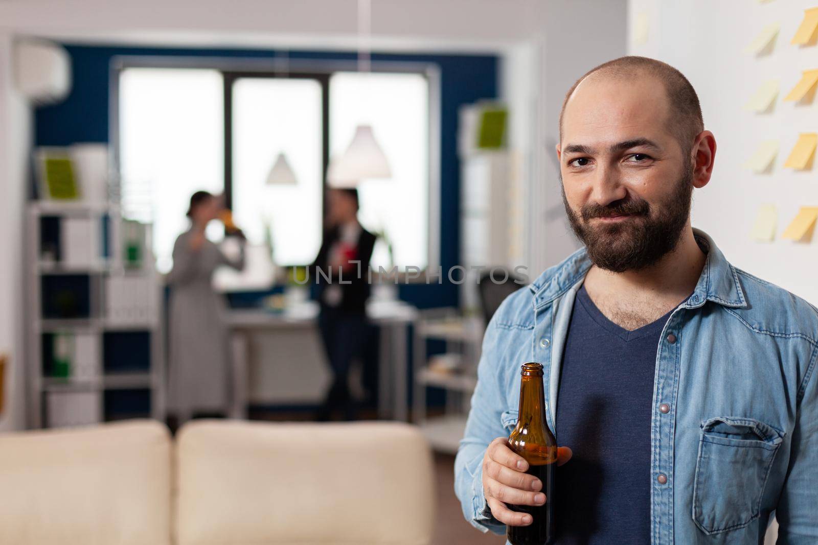 Caucasian man smiling and holding bottle of beer after work by DCStudio