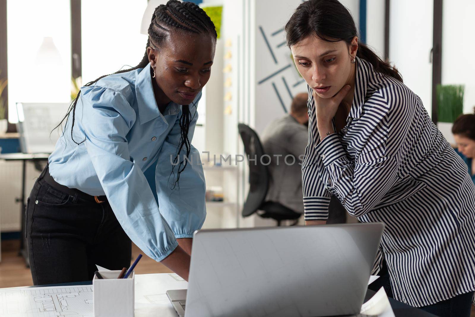 Professional diverse architect women working on laptop computer on blueprint plans for building model maquette. Multi ethnic team at office looking at construction layout project design