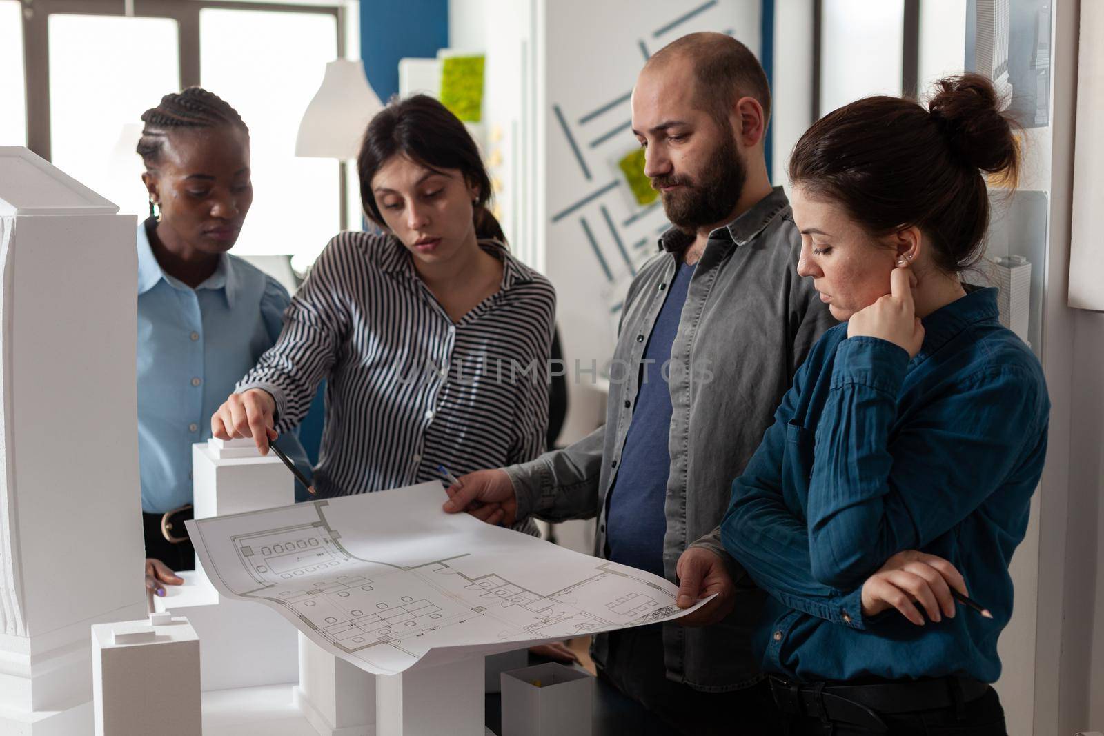 Team of multi ethnic architects designing blueprint plan for construction project design. Workers analyzing maquette buildng model engineering technology at professional office.