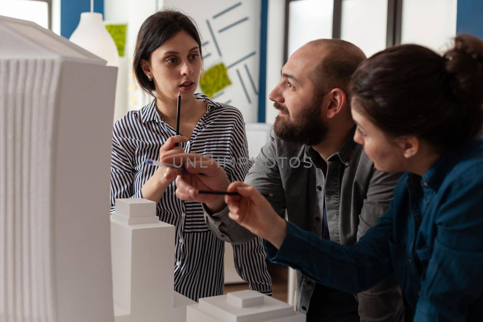 Group of engineer colleagues work in architecture at project with blueprint plans building model maquette. Professional partners discussing vision of construction design on paper