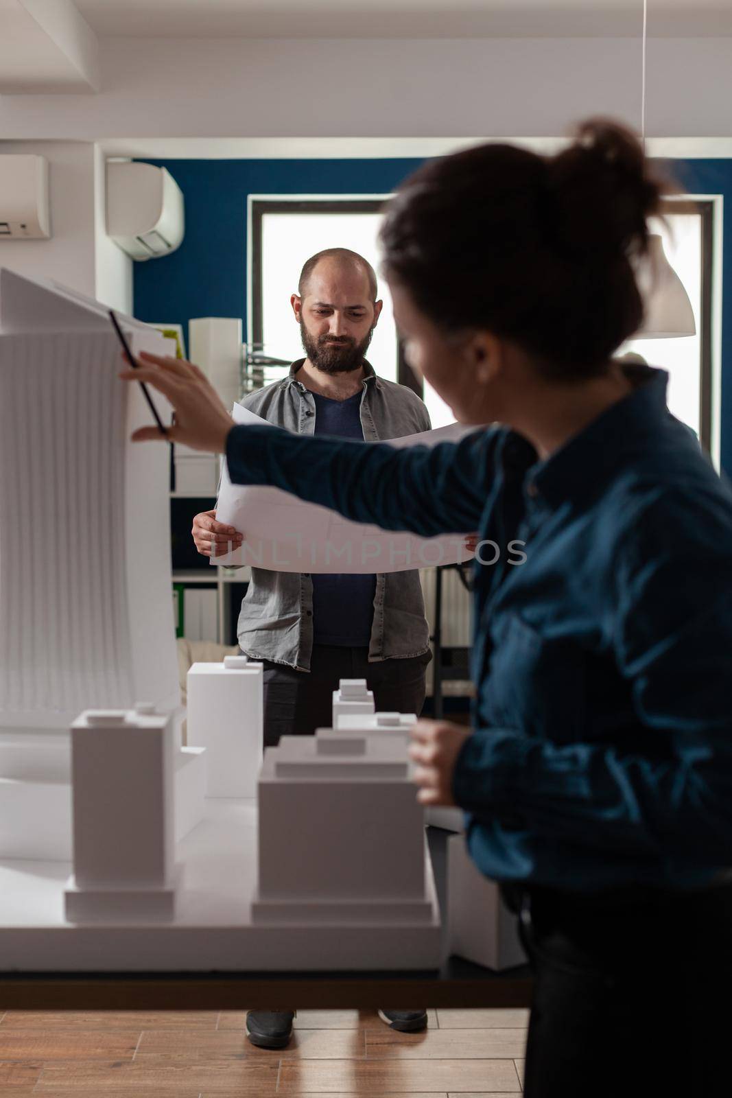 Architecture workers checking blueprints with maquette building model design plan. Caucasian workmates pointing at construction project layout for urban development business