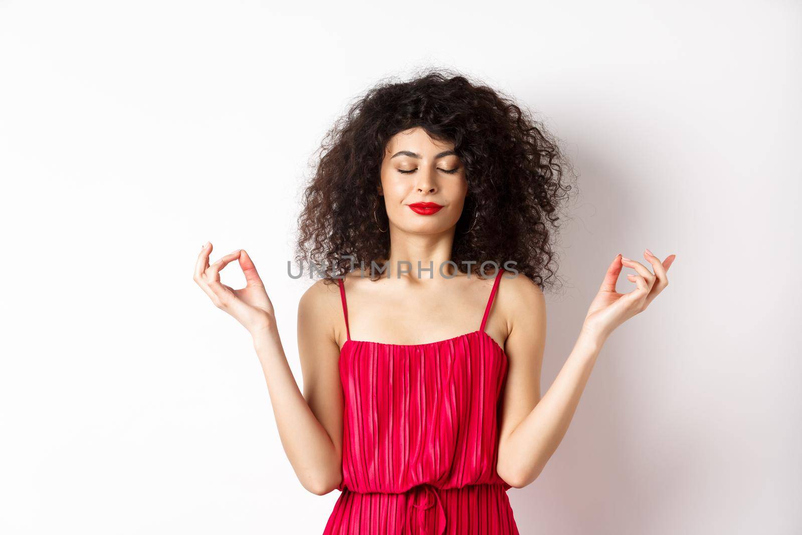 Calm and relaxed smiling woman in red dress, close eyes and meditating, practice yoga in zen pose, standing on white background by Benzoix