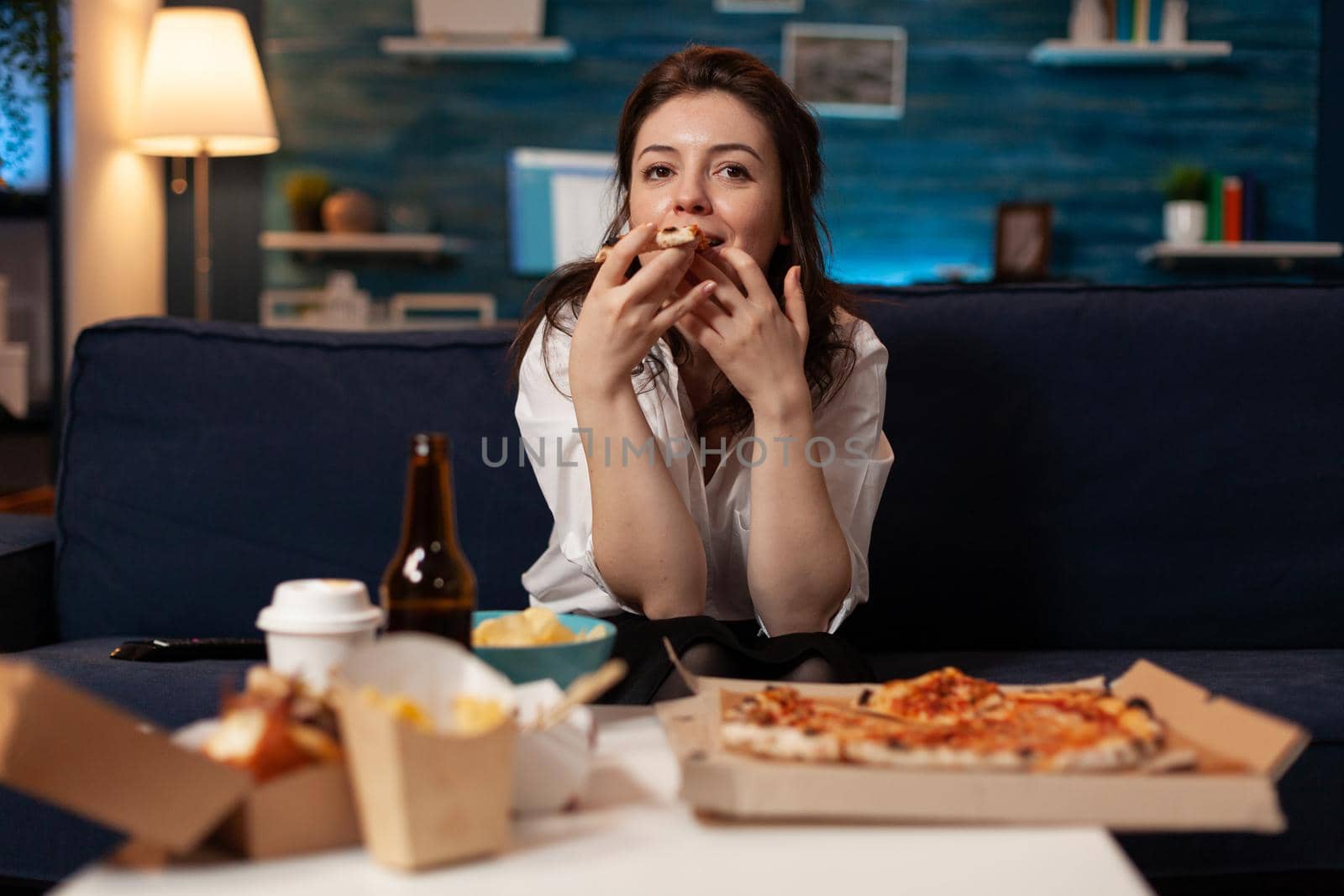 Portrait of woman watching comedy movie eating tasty delivery pizza slice relaxing on sofa by DCStudio
