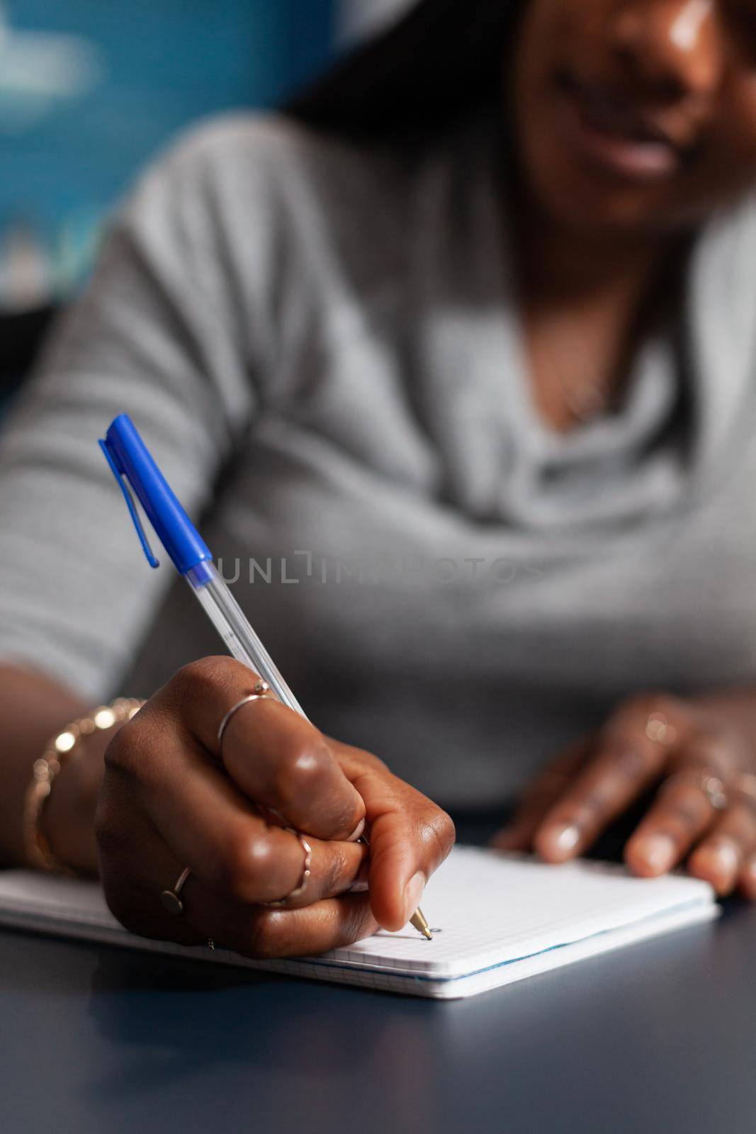 Closeup of black student hands writing university homework during online communication lesson by DCStudio