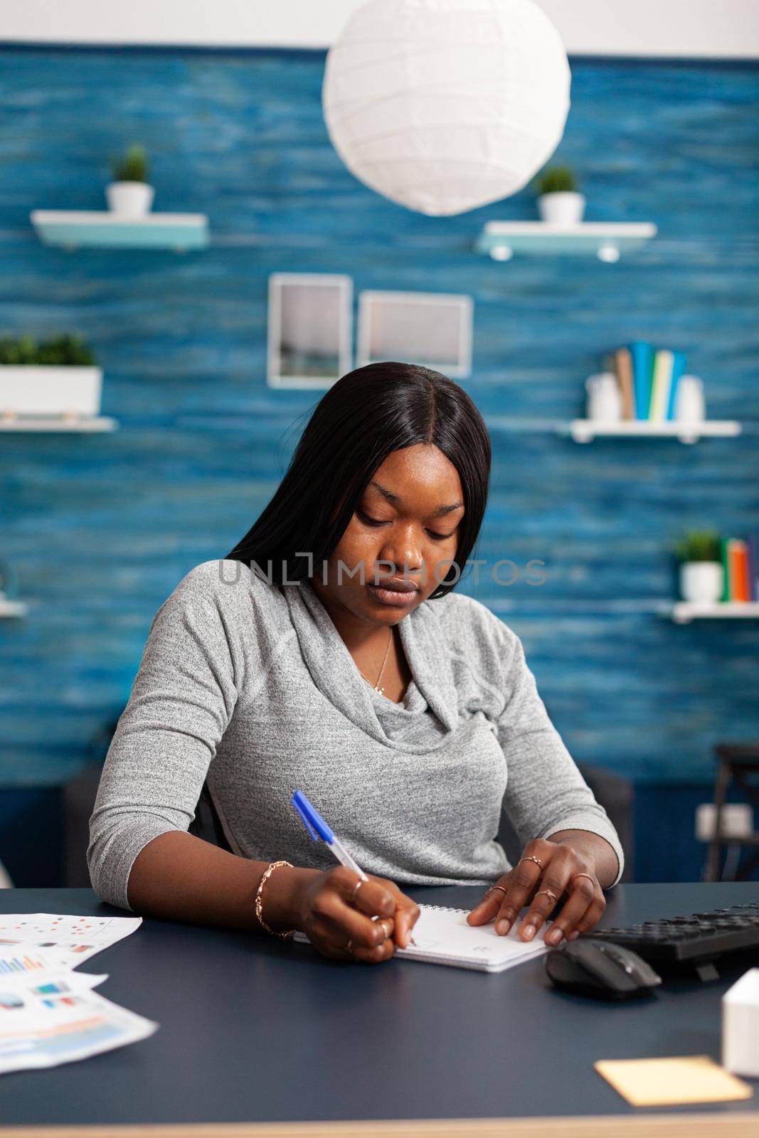 African american student working remote from home studying math lesson writing academic homework on notebook. Black student sitting at desk in living room during university education webinar